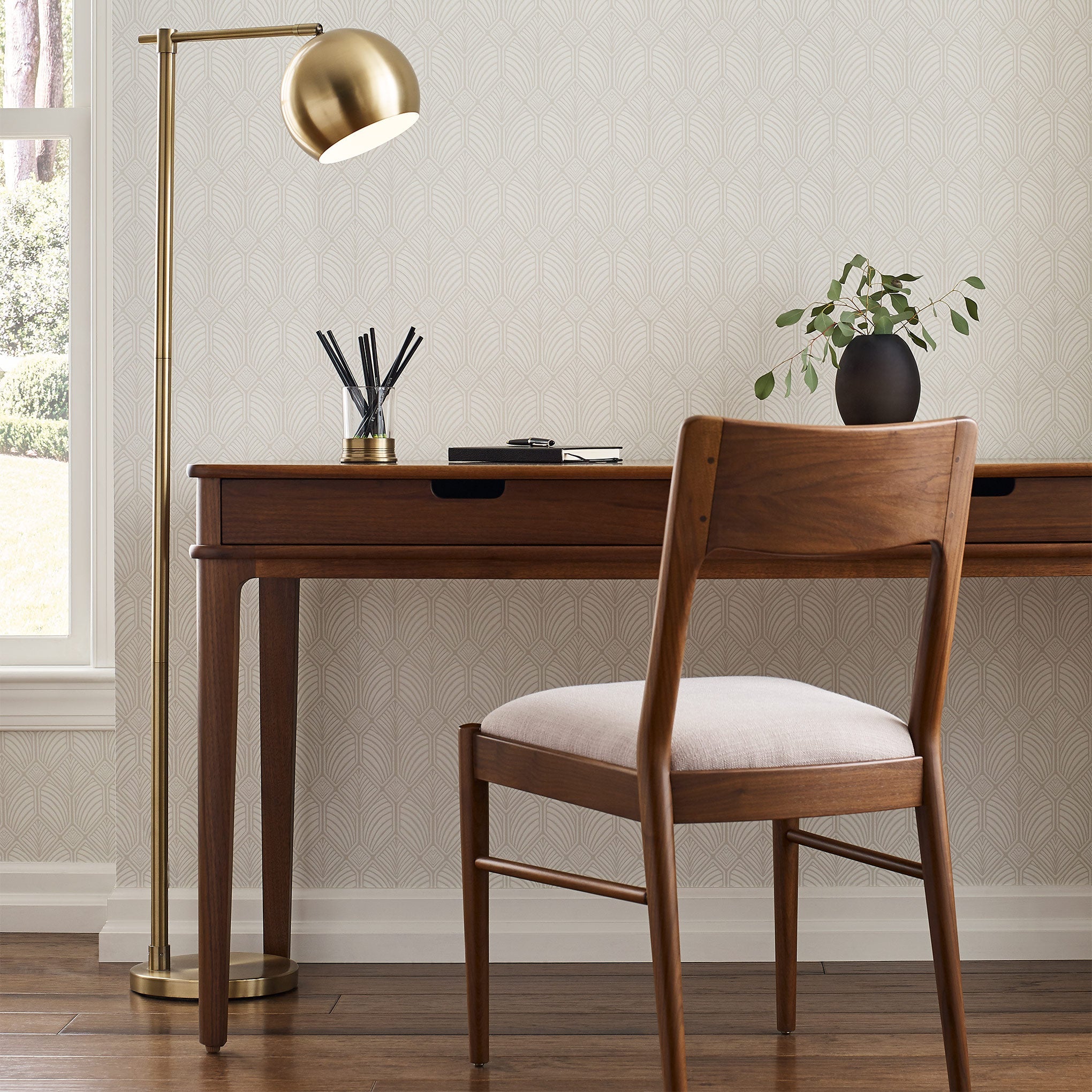 Wooden desk with chair, lamp, and decor items in a room with light-colored walls.