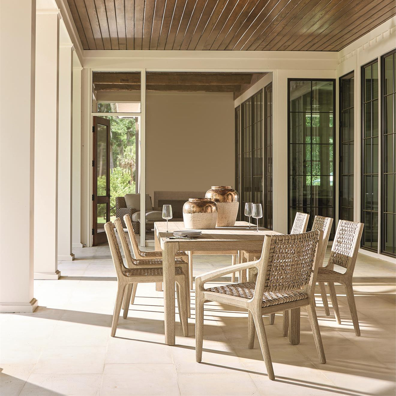 The Edenton dining table set in an outdoor dining space, surrounded by woven dining chairs, with natural light accentuating its elegant and contemporary design.