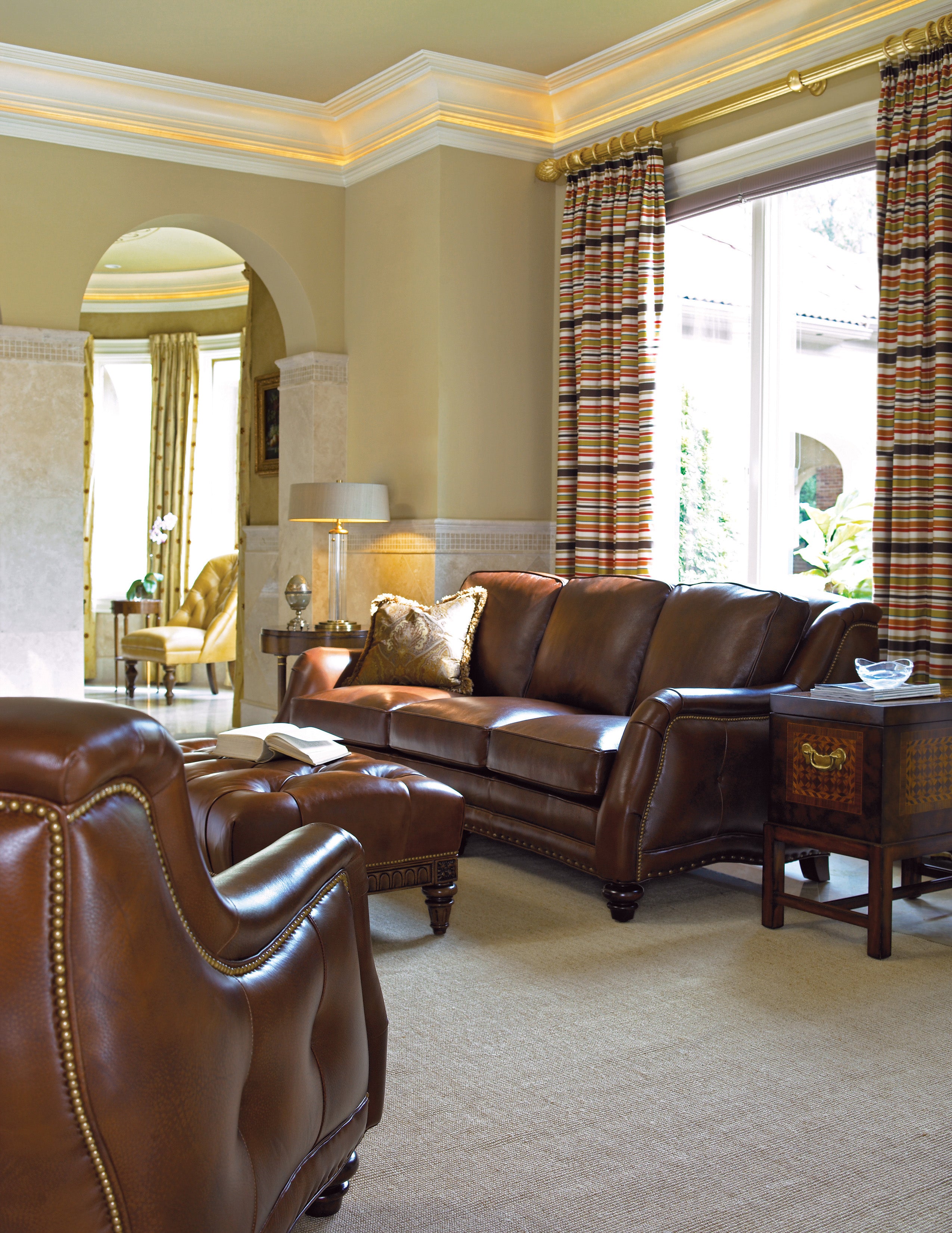 Luxurious living room with brown leather sofa and armchair, striped curtains, and a lamp.
