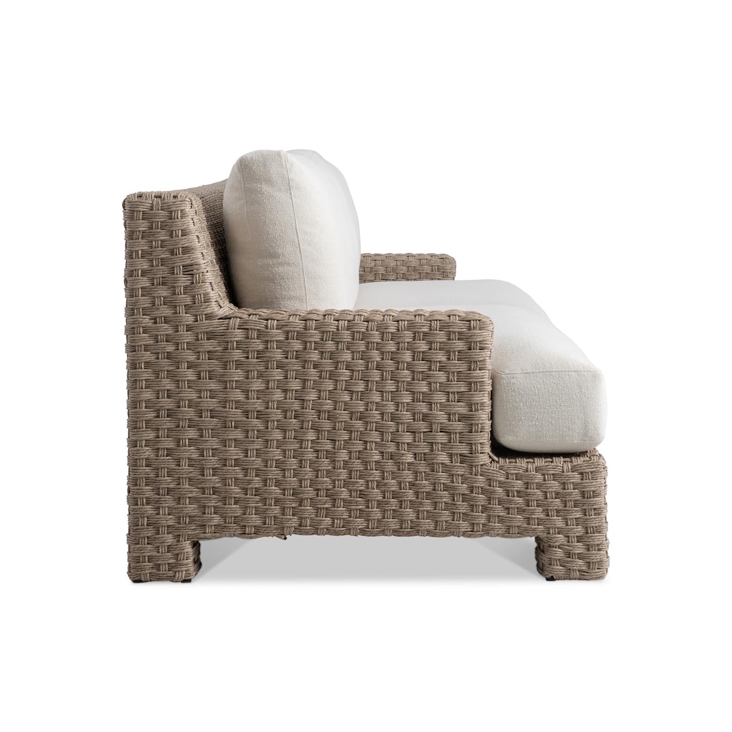A side profile of the outdoor sofa, highlighting the intricate all-weather wicker weave and generously cushioned seating. The wide armrest provides additional comfort and support.