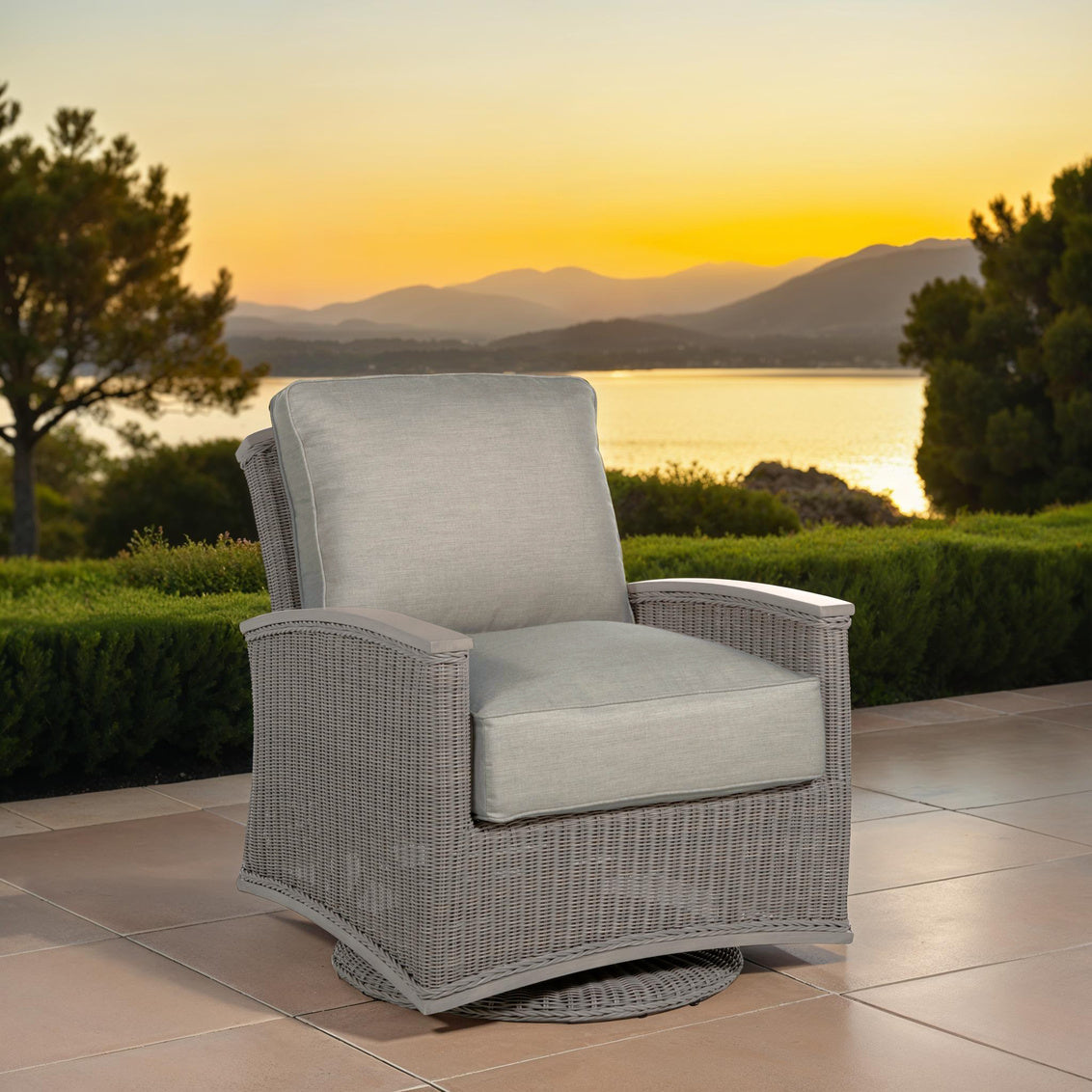 Gray wicker chair with cushions on a patio with a scenic view of mountains and sunset.