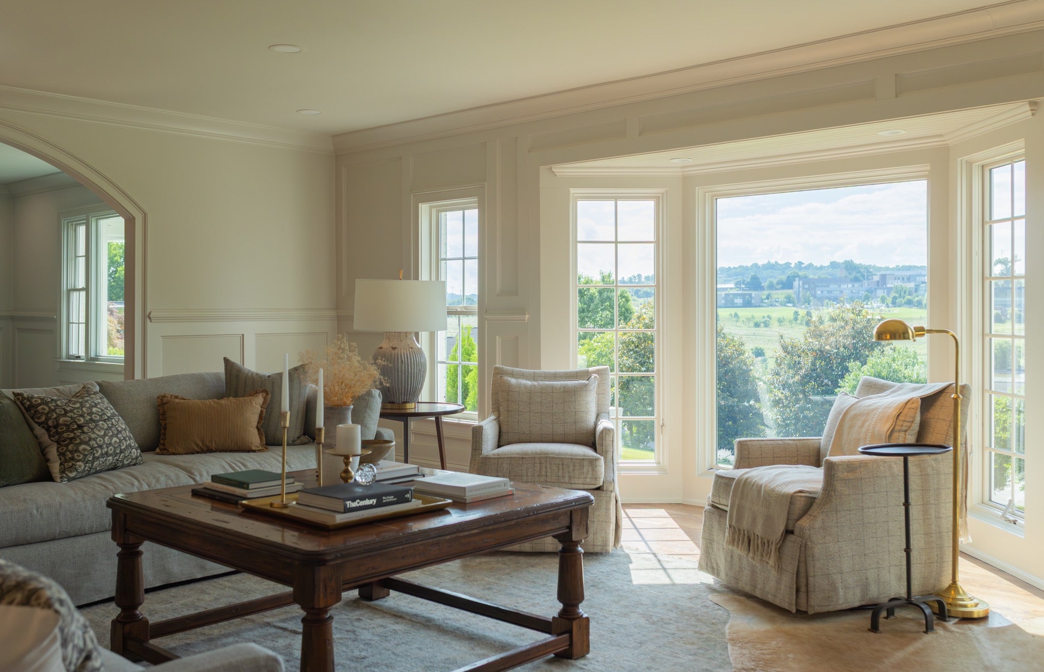 Living room sitting area with skirted chairs framing a green countryside view through a bay window