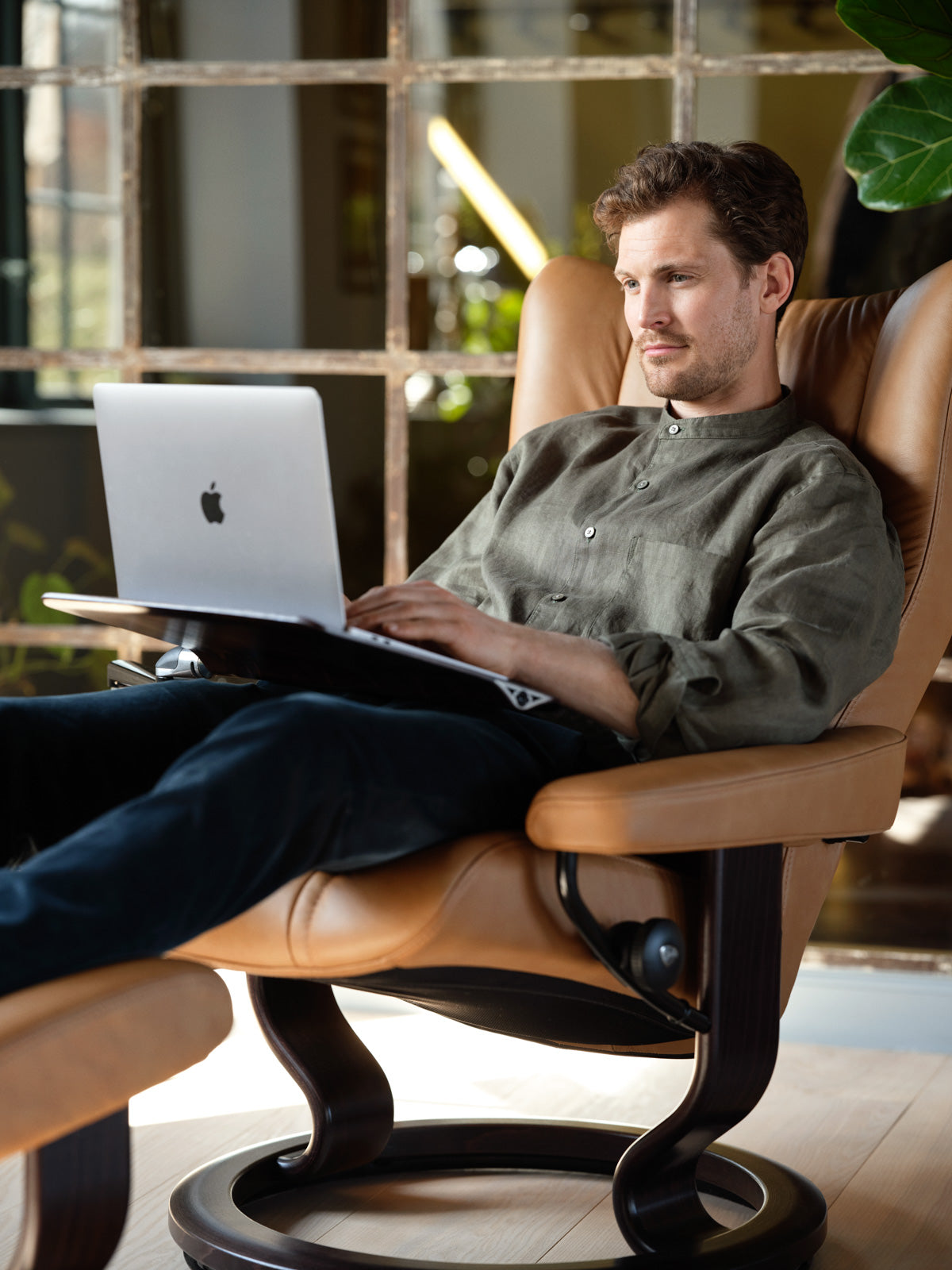 Man working on a laptop in a Stressless Wing office chair with computer table attachment